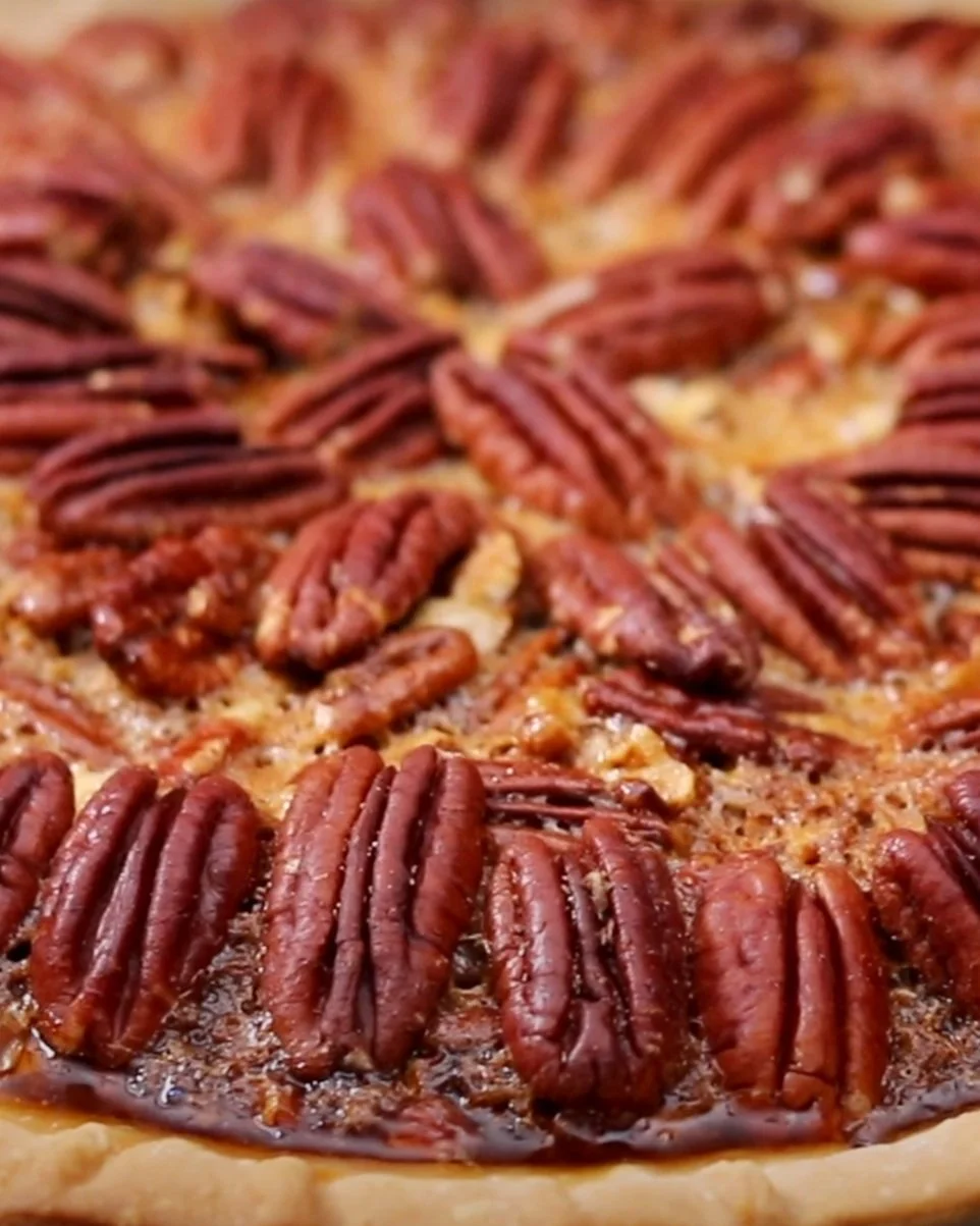 Close-up of a pecan pie with a golden crust and glazed pecans on top.