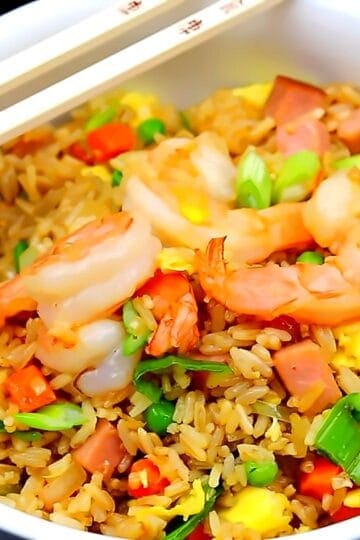 Shrimp fried rice with shrimp, ham, peas, carrots, and scallions in a white bowl with chopsticks