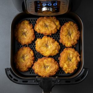 Smashed tostones in air fryer basket mid-cook, golden and crispy