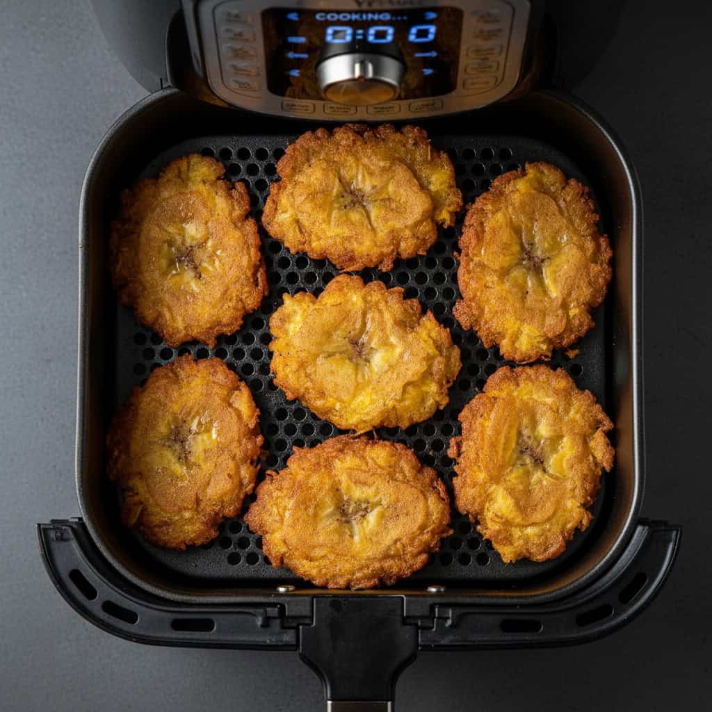 Smashed tostones in air fryer basket mid-cook, golden and crispy