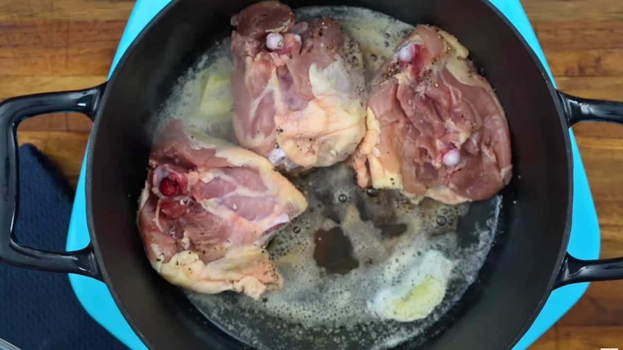 Seasoned bone-in chicken thighs searing in melted butter inside a black Dutch oven