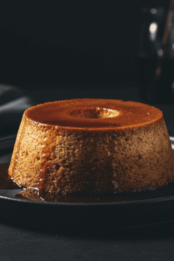 Unmolded Dominican flan de pan on a ceramic plate with dark amber caramel sauce