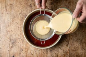 Custard being strained into flanera over caramel for flan dominicano