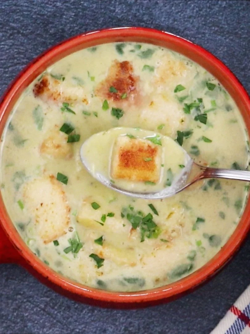 Bowl of creamy potato soup topped with green herbs and croutons