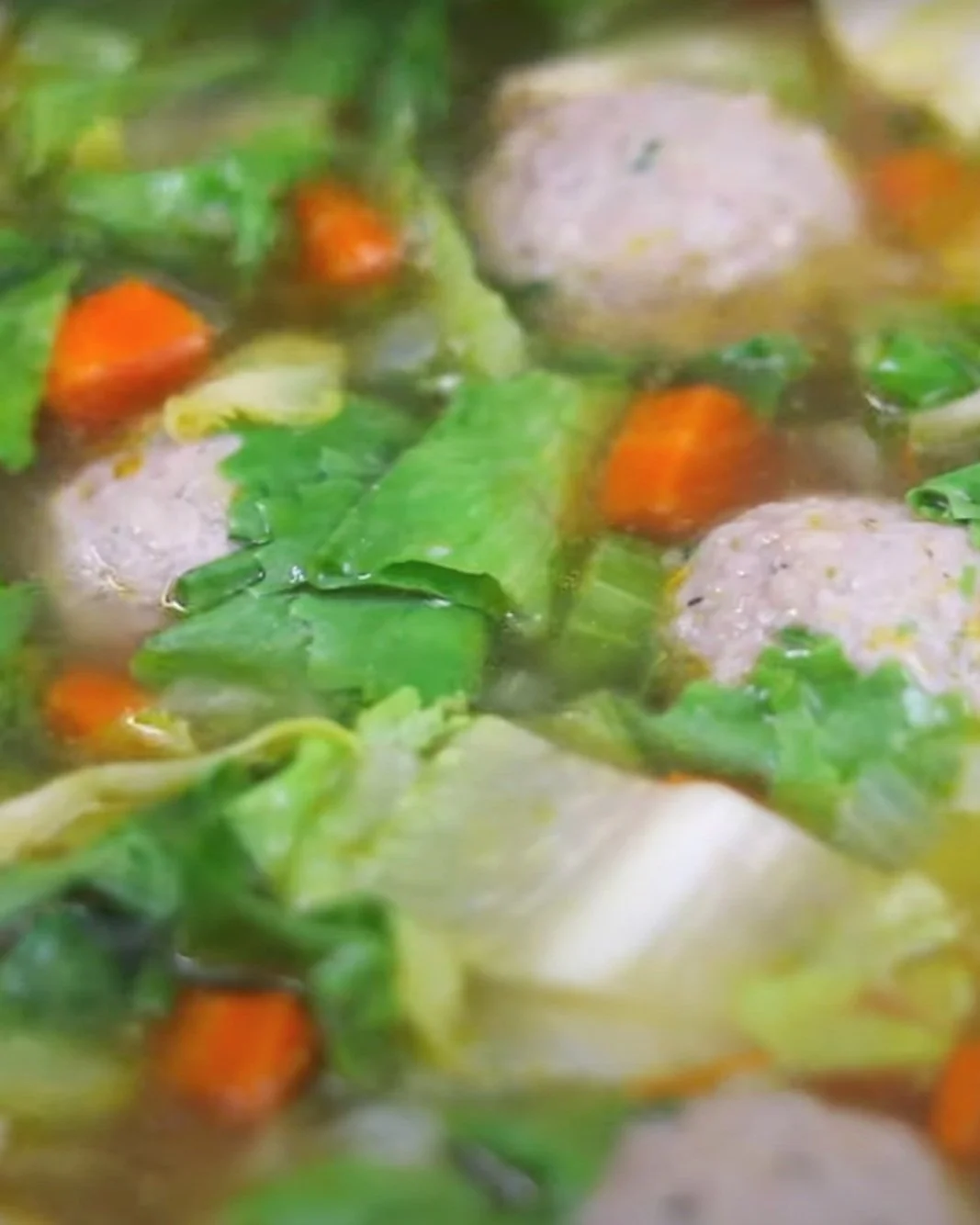Close-up of soup with meatballs, carrots, and leafy greens