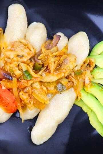 Guanimos con bacalao served on a black plate with sliced avocado
