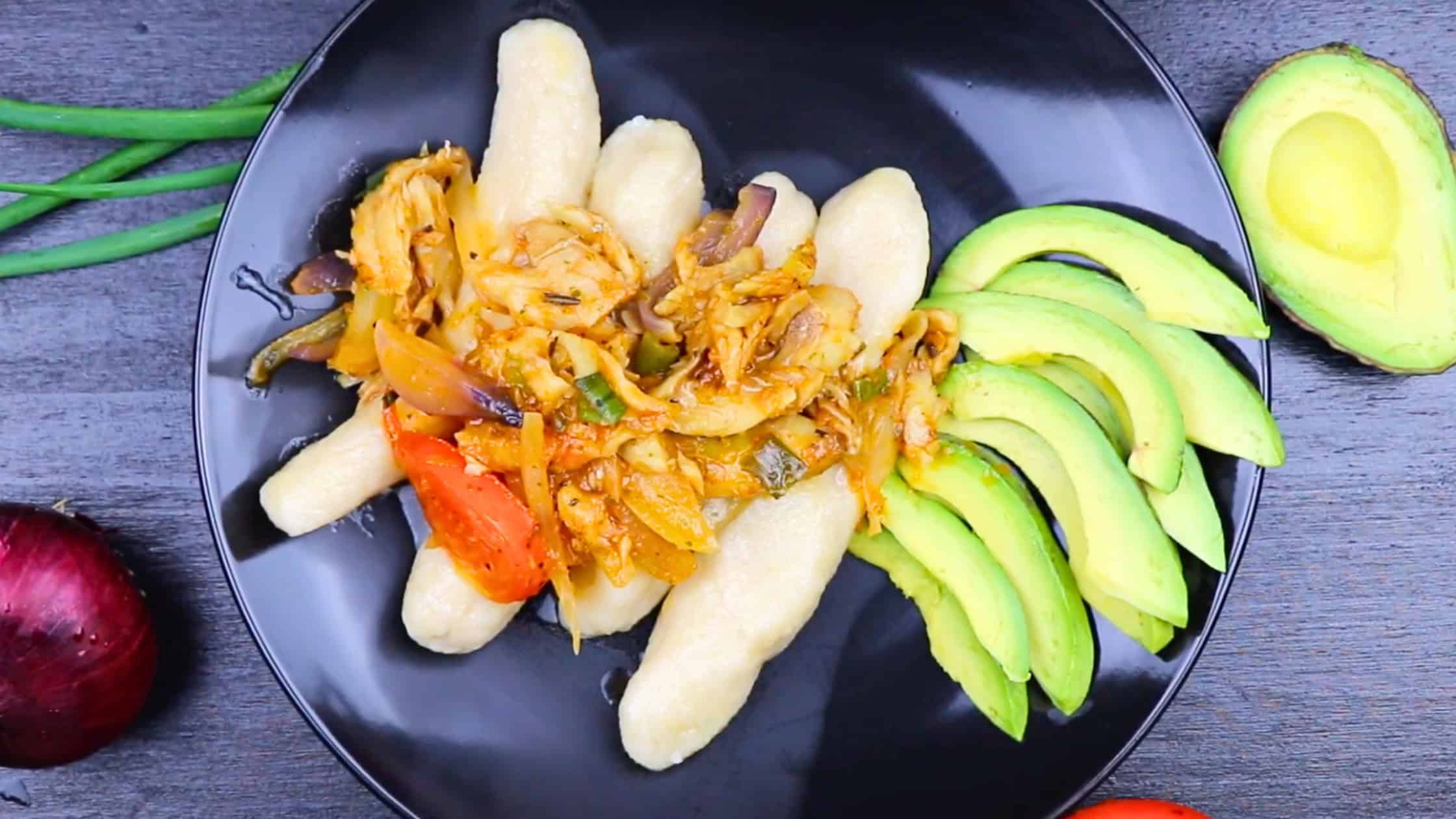 Guanimos con bacalao served on a black plate with sliced avocado