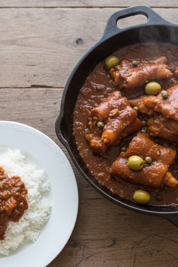 Dominican braised pig feet in a cast iron caldero with rich sauce olives and white rice