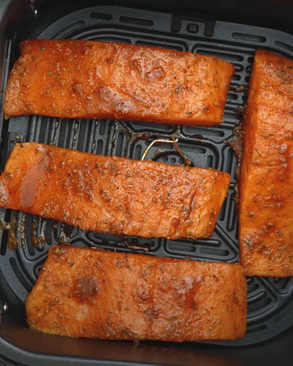 Salmon fillets cooking in an air fryer basket with golden brown blackening crust