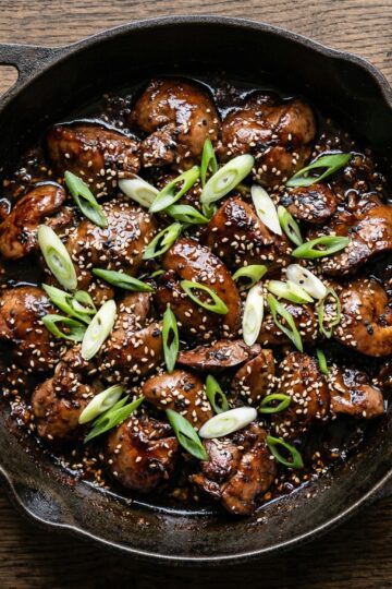 Sticky glazed chicken livers in a cast iron skillet with scallions and sesame seeds