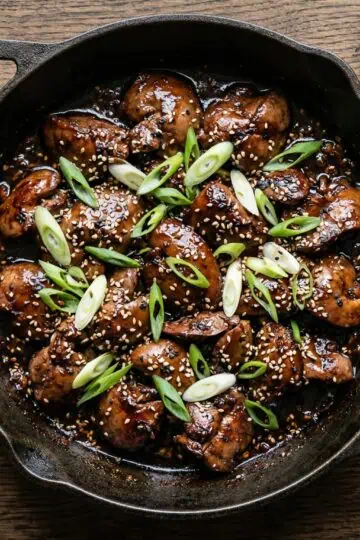 Sticky glazed chicken livers in a cast iron skillet with scallions and sesame seeds