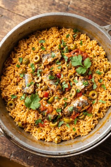 Locrio de pica-pica served in a large pot showing fluffy rice studded with spicy sardines, olives, and fresh cilantro