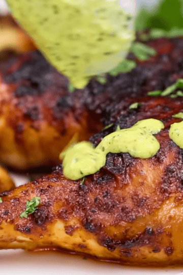 Golden crispy oven baked Peruvian chicken leg quarters on a white plate with aji verde green sauce and fresh lime