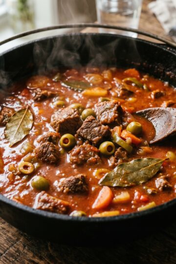 Dominican stewed beef in caldero with tomato sauce olives and bay leaf