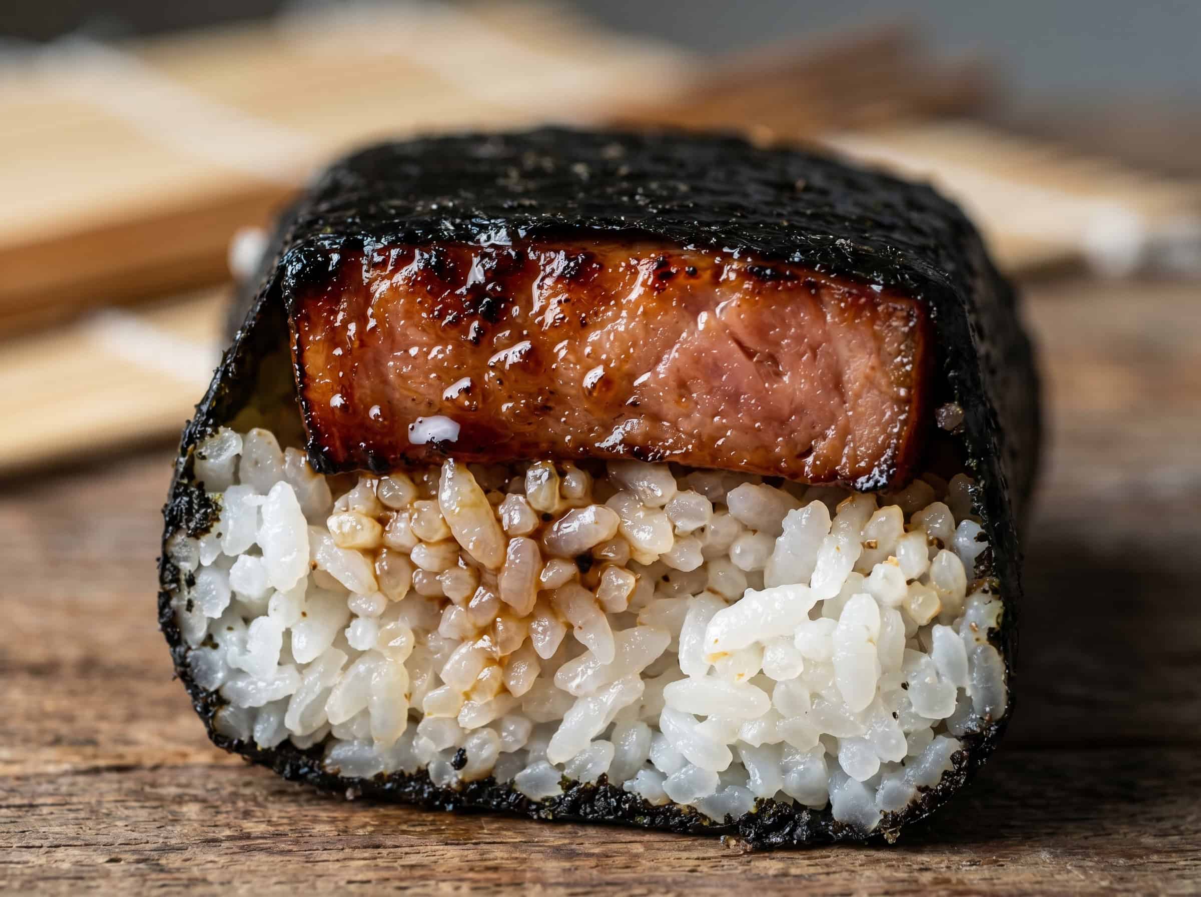 Macro texture detail of spam musubi showing individual grains of sticky rice, glossy teriyaki glaze on the spam, and crisp black nori
