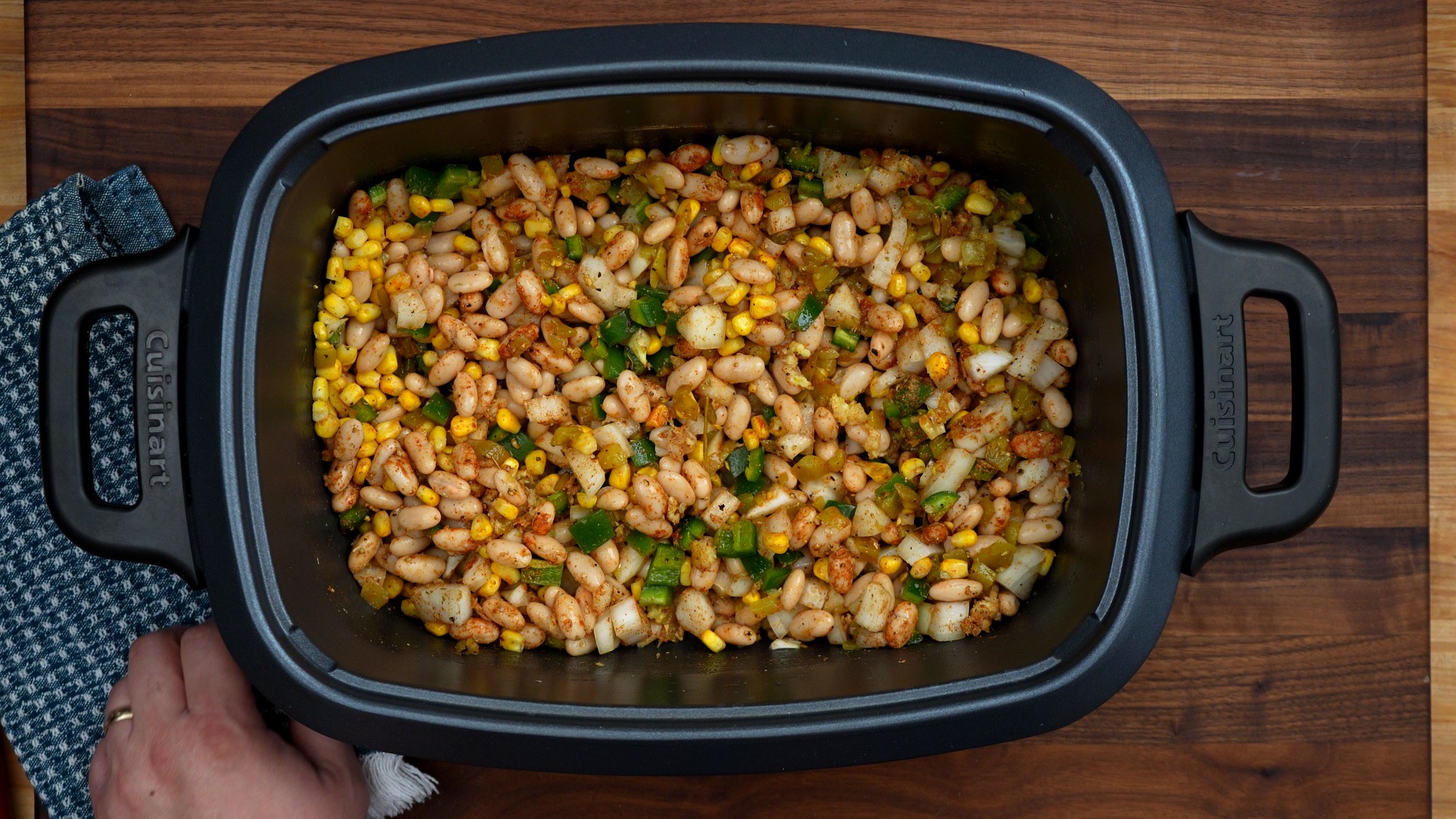 Slow cooker filled with white chicken chili ingredients before cooking: white beans, corn, green chiles, diced onion and seasonings