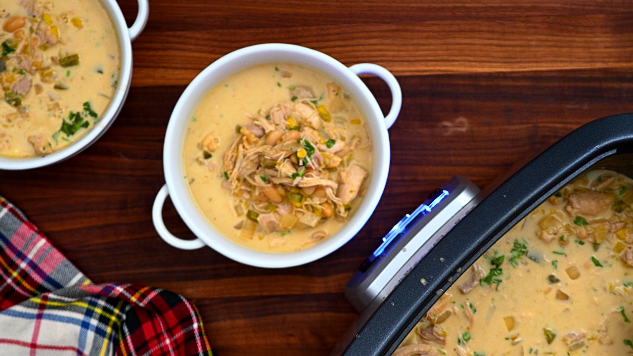 Overhead view of two bowls of slow cooker white chicken chili on a wooden table with a plaid napkin