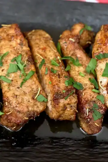 Air fryer country style pork ribs on a black platter with fresh parsley