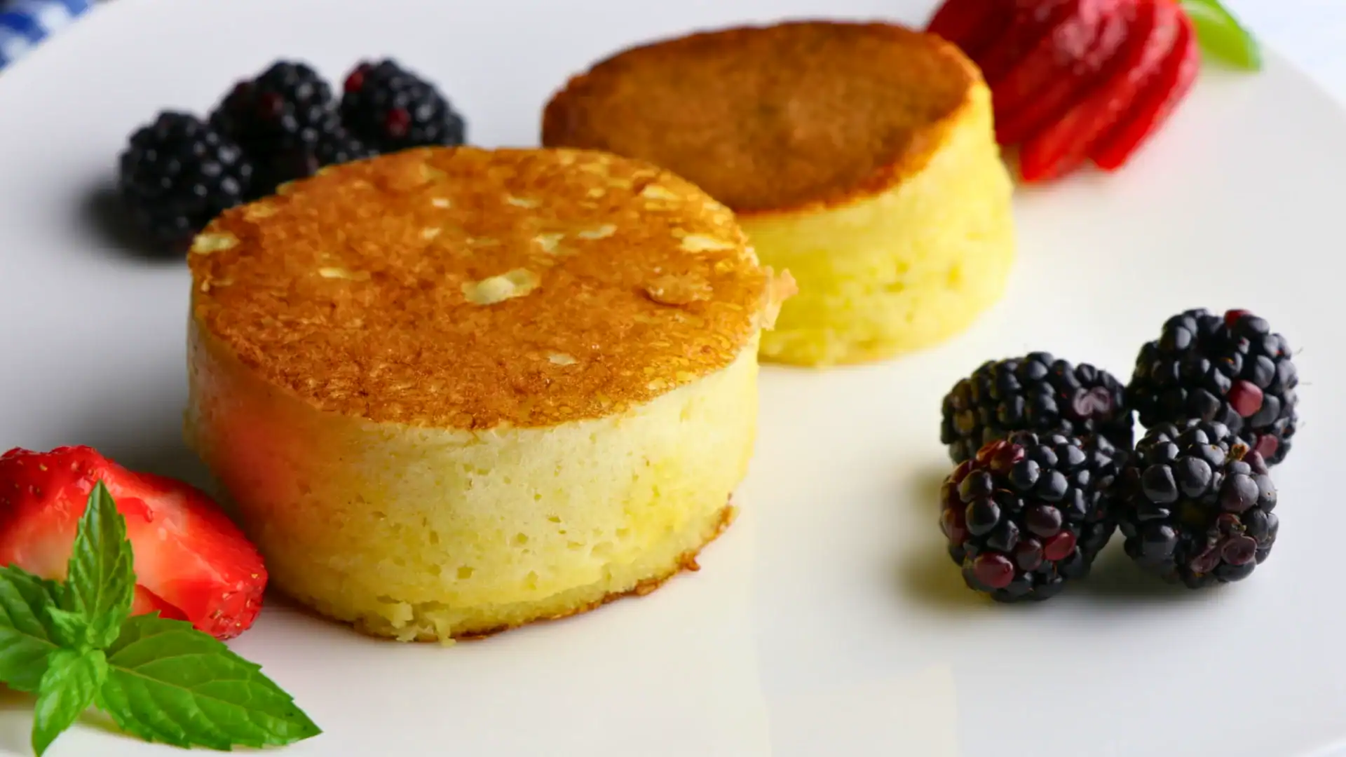 Two fluffy Japanese souffle pancakes on a white plate with fresh strawberries, blackberries, and mint
