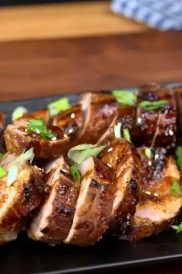 gochujang glazed pork tenderloin on black platter with scallions