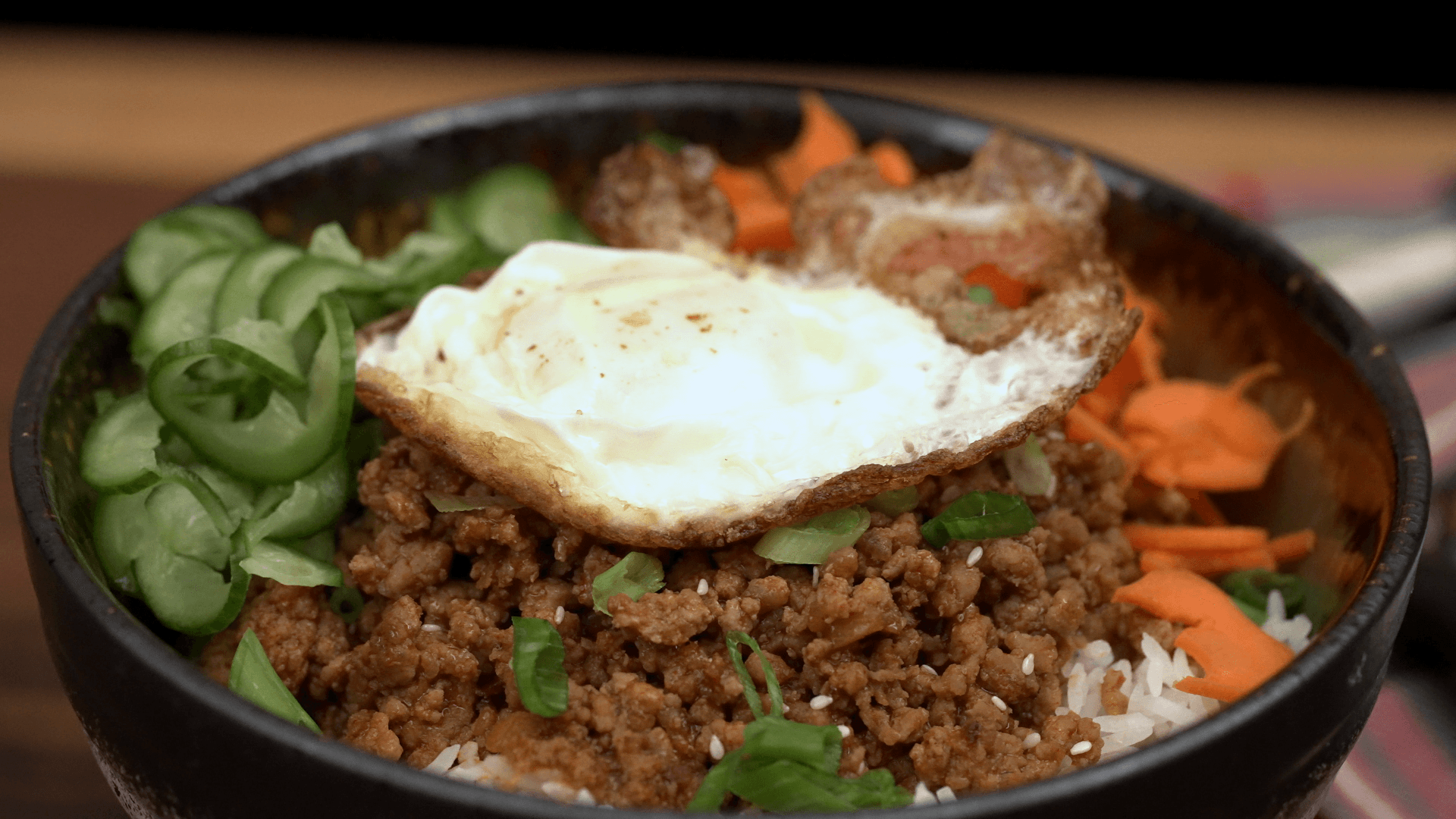 Korean gochujang pork bowl with fried egg, cucumber ribbons, shaved carrots, scallions, and sesame seeds
