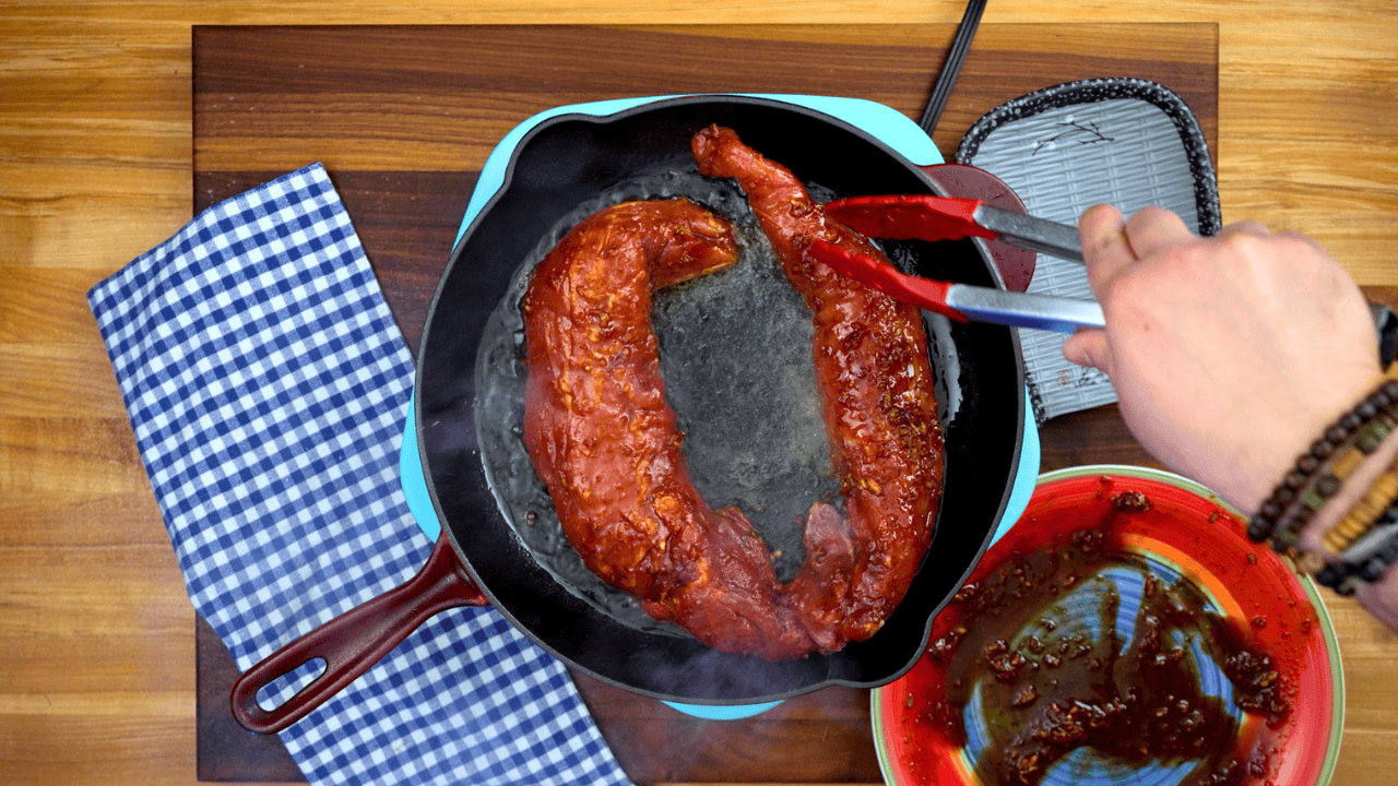 searing gochujang pork tenderloin in cast iron skillet overhead view
