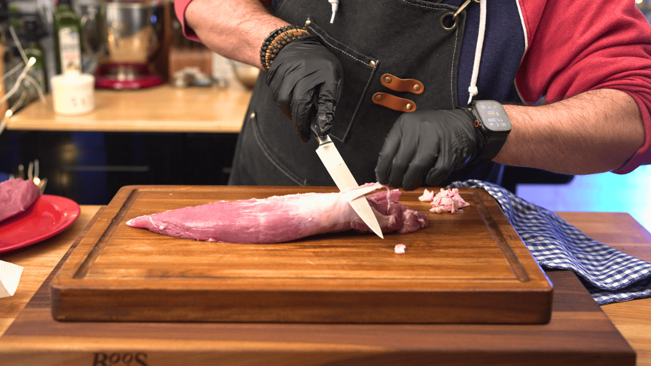 trimming silver skin from pork tenderloin on cutting board
