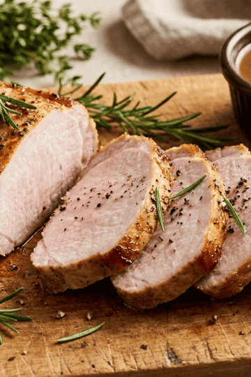 Juicy air fryer pork loin sliced on a wooden cutting board with fresh rosemary garnish
