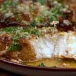 Pan seared Chilean sea bass flaked open showing moist white interior with lemon garlic butter sauce