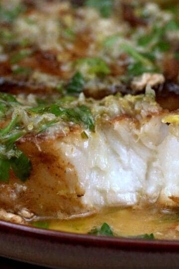 Pan seared Chilean sea bass flaked open showing moist white interior with lemon garlic butter sauce