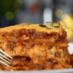 A slice of slow cooker lasagna with layers of pasta, meat sauce, and melted cheese on a white plate