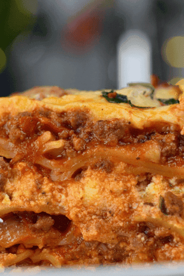 A slice of slow cooker lasagna with layers of pasta, meat sauce, and melted cheese on a white plate