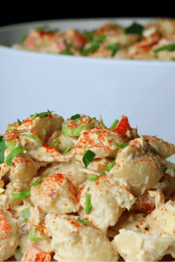Creamy tuna pasta salad with shell pasta, red bell pepper, celery, and paprika on a white plate