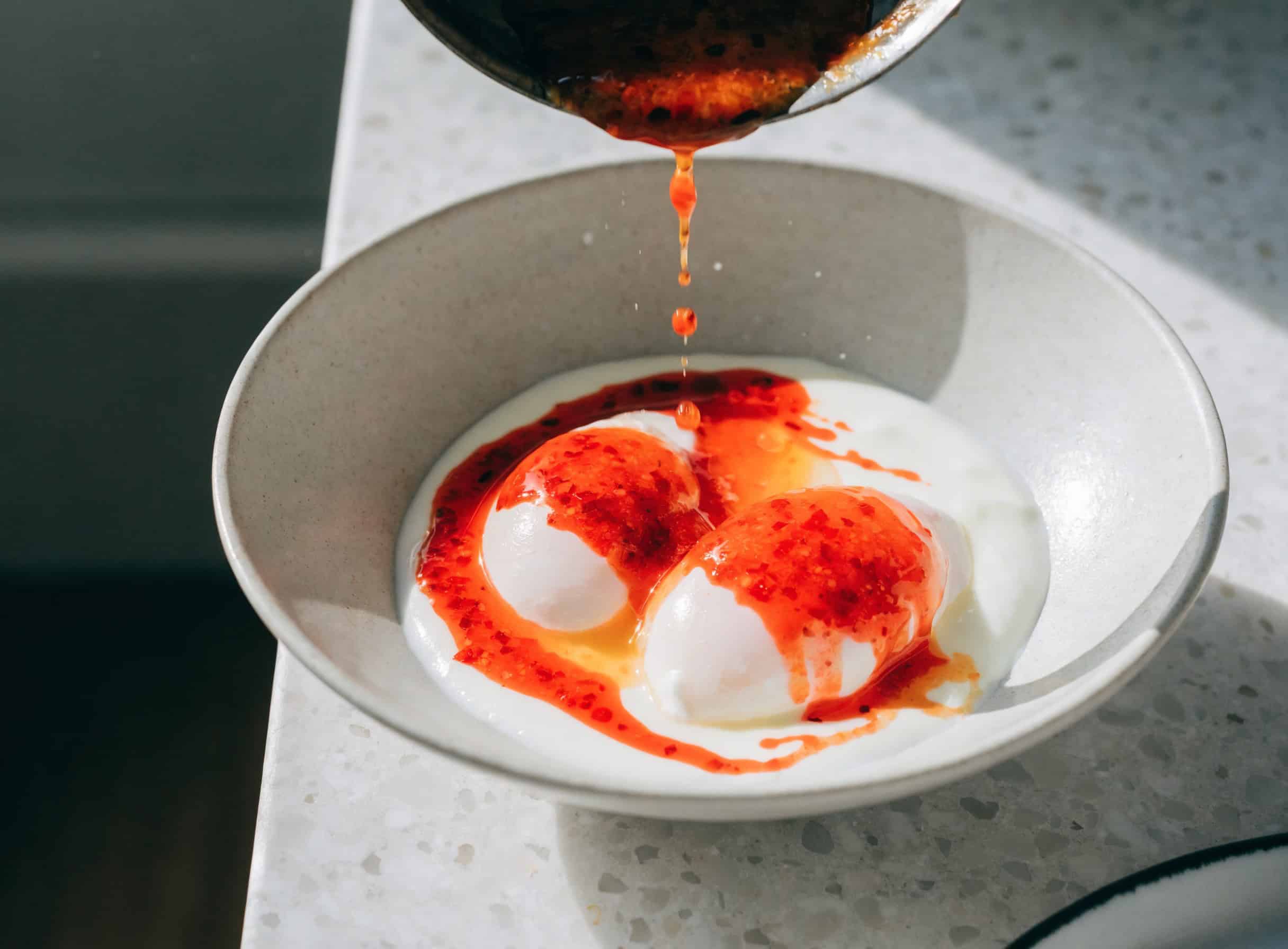 Drizzling Aleppo pepper butter over poached eggs