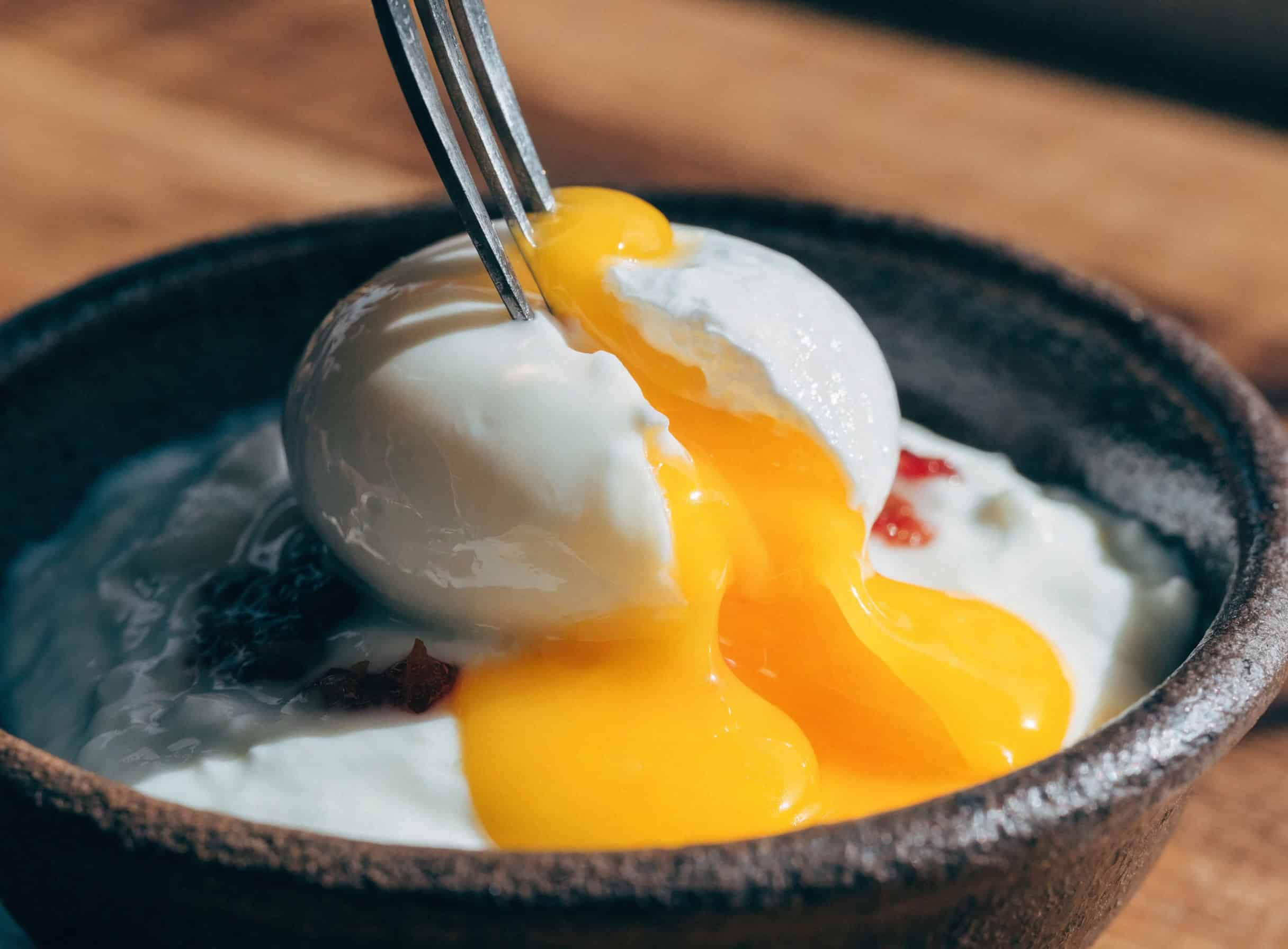 Fork breaking into poached egg with runny yolk